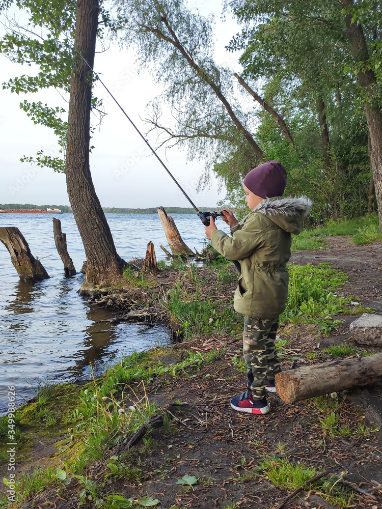 Fototapeta premium The child holds spinning in his hands and spins the coil pulling out a catch. The concept of training a child fishing. The concept of relaxation by the water, river, lake.