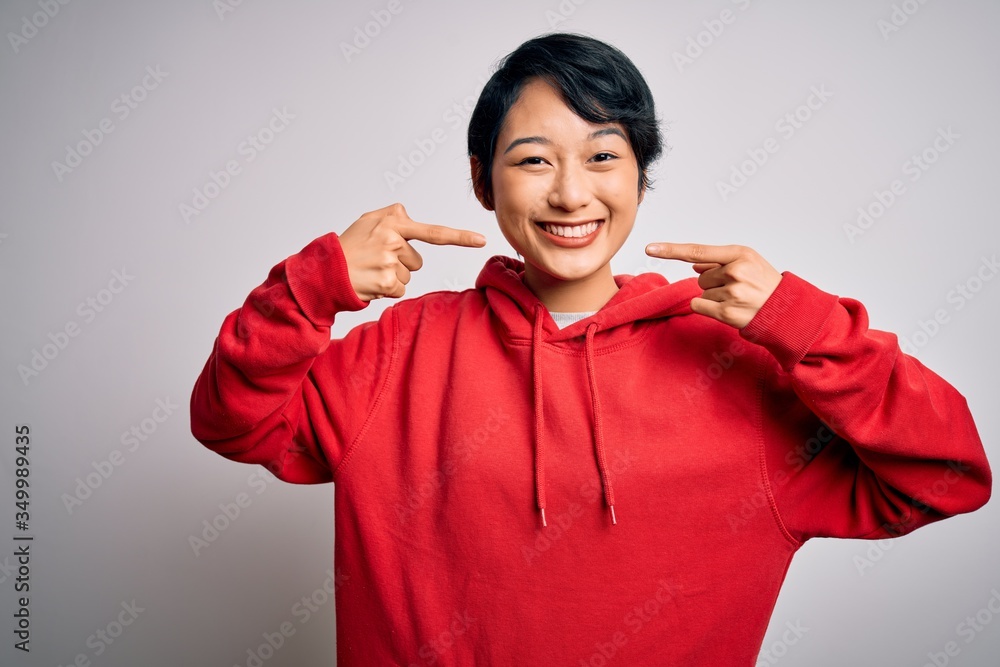 Young beautiful asian girl wearing casual sweatshirt with hoodie over white background smiling cheerful showing and pointing with fingers teeth and mouth. Dental health concept. Young beautiful asian girl wearing casual sweatshirt with hoodie over white background smiling cheerful showing and pointing with fingers teeth and mouth. Dental health concept.