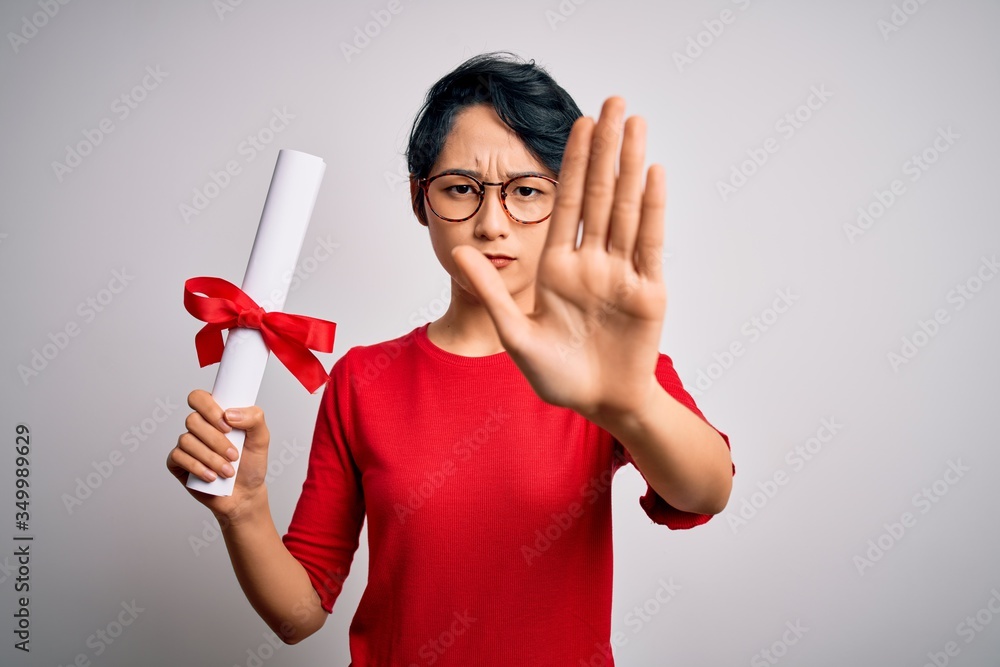 Beautiful chinese student woman wearing glasses holding university graduated diploma degree with open hand doing stop sign with serious and confident expression, defense gesture Beautiful chinese student woman wearing glasses holding university graduated diploma degree with open hand doing stop sign with serious and confident expression, defense gesture