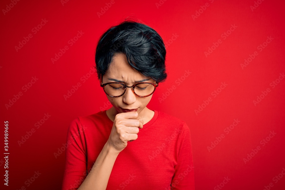 Young beautiful asian girl wearing casual t-shirt and glasses over isolated red background feeling unwell and coughing as symptom for cold or bronchitis. Health care concept. Young beautiful asian girl wearing casual t-shirt and glasses over isolated red background feeling unwell and coughing as symptom for cold or bronchitis. Health care concept.