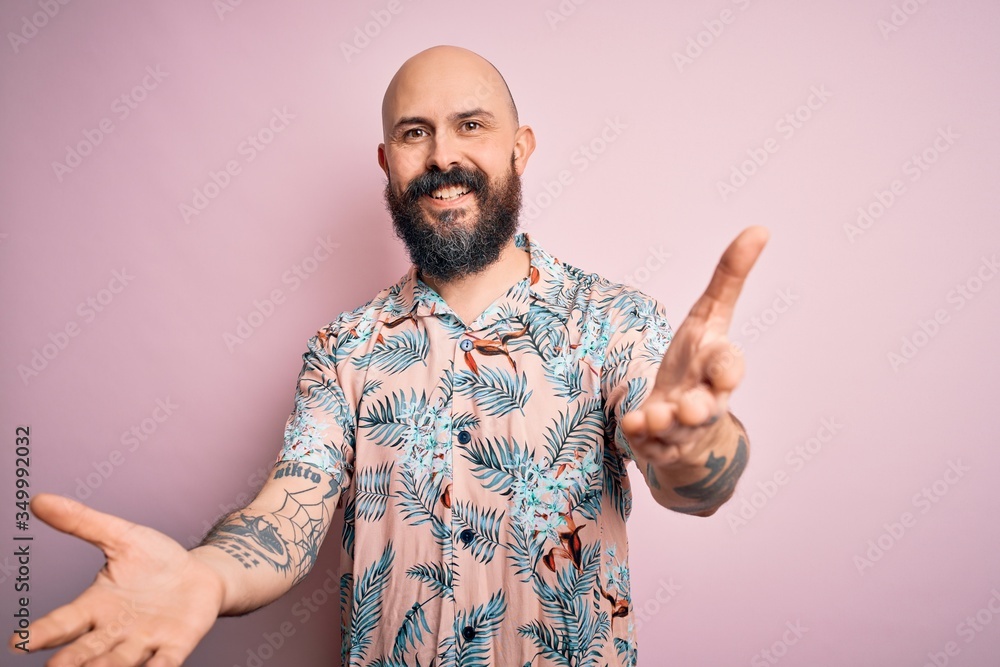 Handsome bald man with beard and tattoo wearing casual floral shirt over pink background smiling cheerful offering hands giving assistance and acceptance. Handsome bald man with beard and tattoo wearing casual floral shirt over pink background smiling cheerful offering hands giving assistance and acceptance.