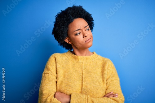 Young beautiful African American afro woman with curly hair wearing yellow casual sweater looking to the side with arms crossed convinced and confident