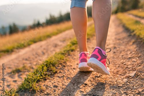 Walking or running legs on mountain road, adventure and exercising in summer nature. Runner girl jogging feet closeup running shoes banner panorama. Lifestyle adventure vacations concept
