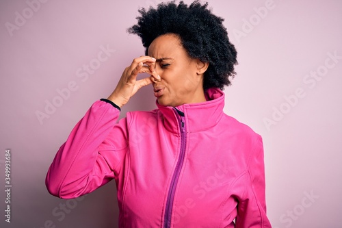 Young African American afro sportswoman with curly hair wearing sportswear doin sport smelling something stinky and disgusting, intolerable smell, holding breath with fingers on nose. Bad smell