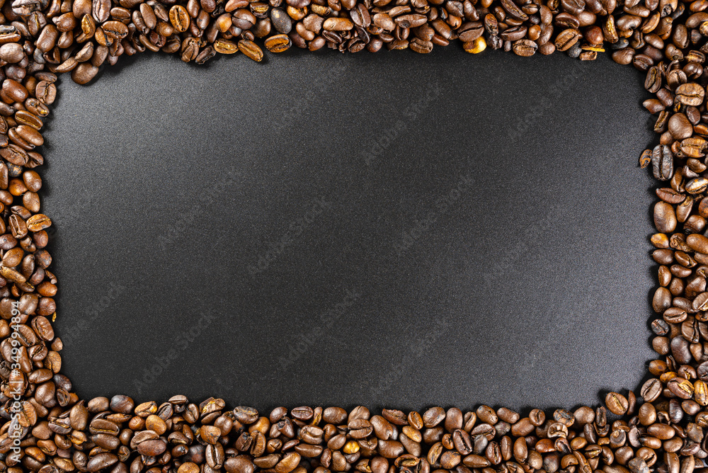 Background made of fresh roasted coffee beans lying flat on a black background with copy space in the shape of a rectangle.