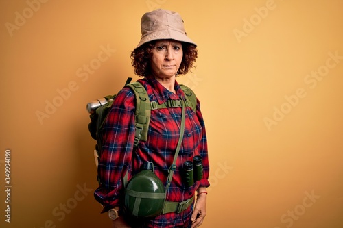Middle age curly hair hiker woman hiking wearing backpack and water canteen using binoculars skeptic and nervous, frowning upset because of problem. Negative person.