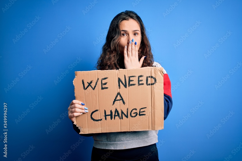 Young beautiful activist woman holding banner with change message over blue background cover mouth with hand shocked with shame for mistake, expression of fear, scared in silence, secret concept Young beautiful activist woman holding banner with change message over blue background cover mouth with hand shocked with shame for mistake, expression of fear, scared in silence, secret concept