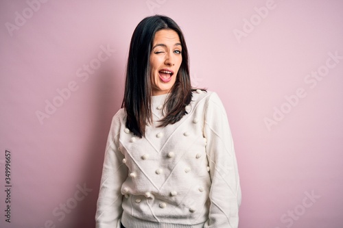 Young brunette woman with blue eyes wearing casual sweater over isolated pink background winking looking at the camera with sexy expression, cheerful and happy face. © Krakenimages.com