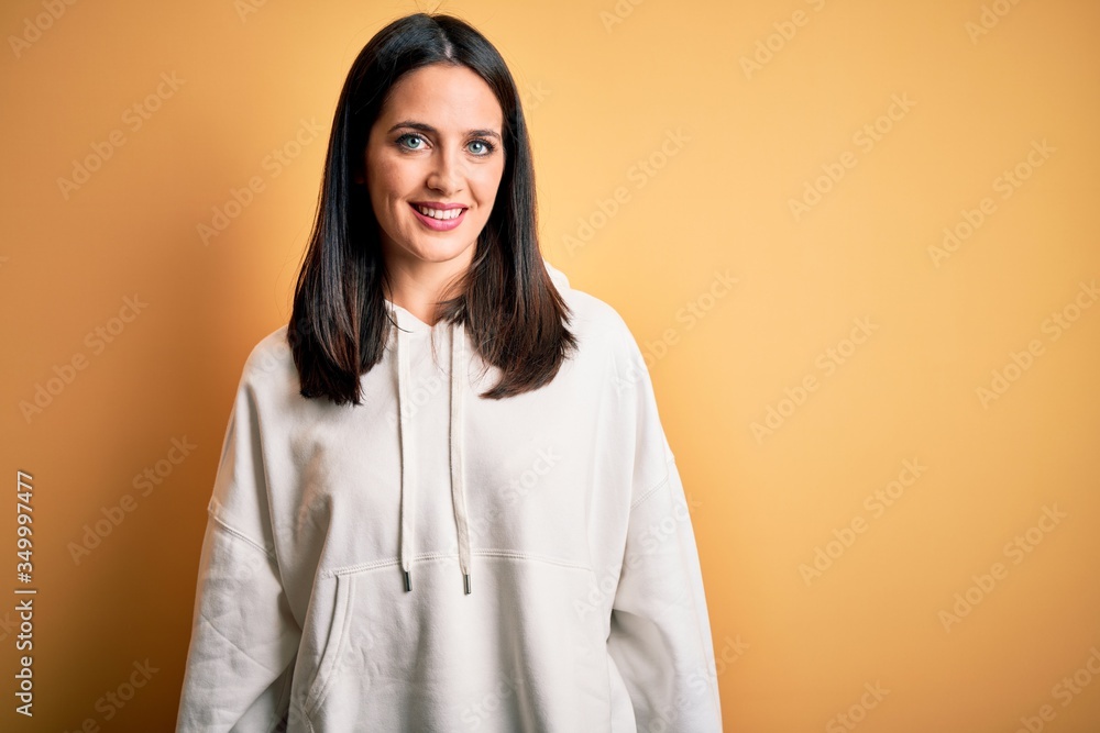 Young brunette sportswoman with blue eyes wearing training sweatshirt over yellow background with a happy and cool smile on face. Lucky person. Young brunette sportswoman with blue eyes wearing training sweatshirt over yellow background with a happy and cool smile on face. Lucky person.