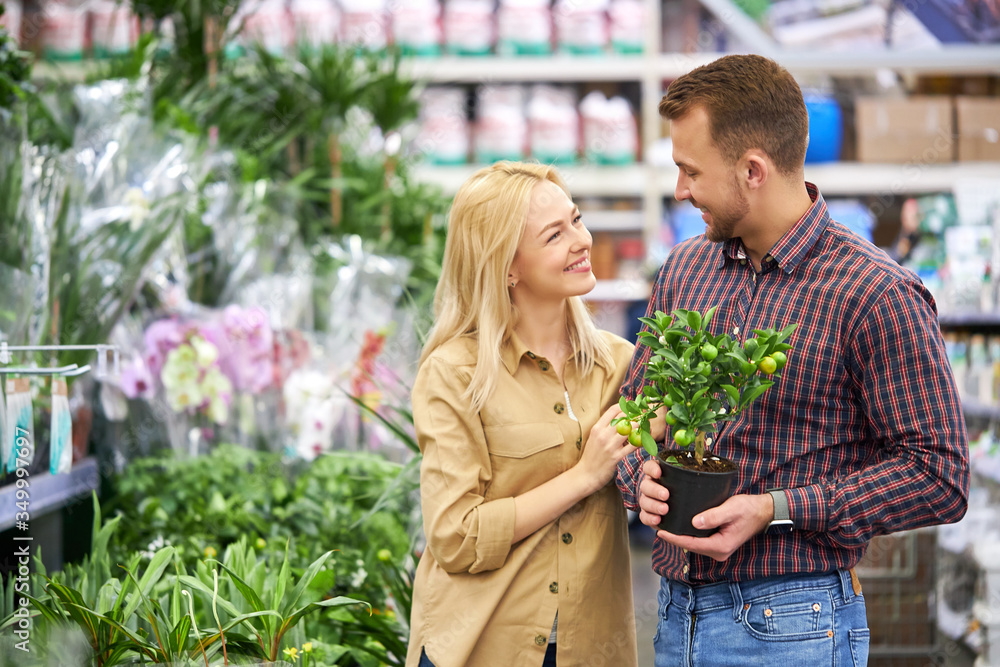 portrait of good-looking caucasian couple looking for flowers in pots, they equip their empty room into a beautiful room full of flowers. look at each other with love, smile