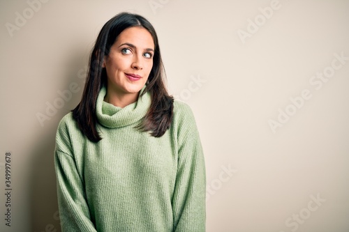Young brunette woman with blue eyes wearing turtleneck sweater over white background smiling looking to the side and staring away thinking.
