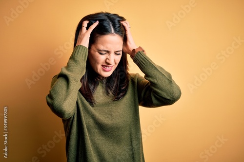 Young brunette woman with blue eyes wearing green casual sweater over yellow background suffering from headache desperate and stressed because pain and migraine. Hands on head. © Krakenimages.com