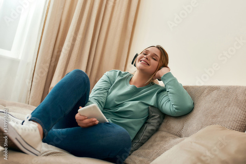 Chilling out. Young and happy beautiful girl in casual clothes wearing headphones, relaxing on sofa and listening music