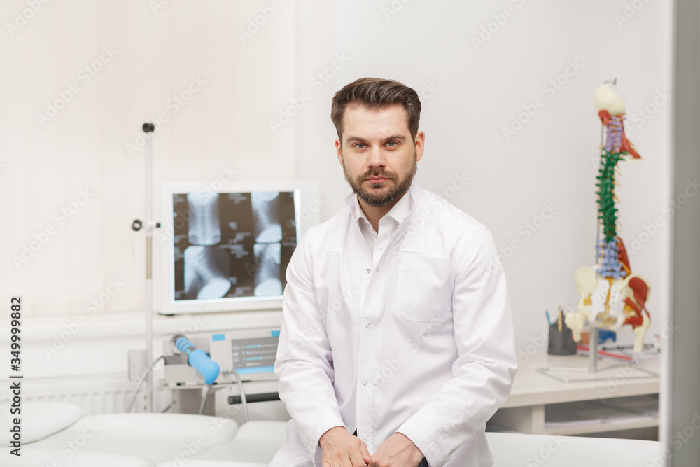 Portrait of doctor in white coat at workplace with medical staff on the background. Male doctor working at office desk. Medical office, clinic.