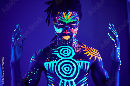 Schilderij op canvas portrait of african man painted in fluorescent paint on face and muscular torso, studio shot with UV light