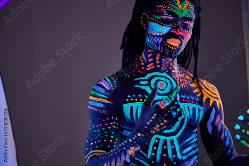 portrait of muscular young man in bright blacklight bodyart glowing in darkness. fluorescent, luminescent body art