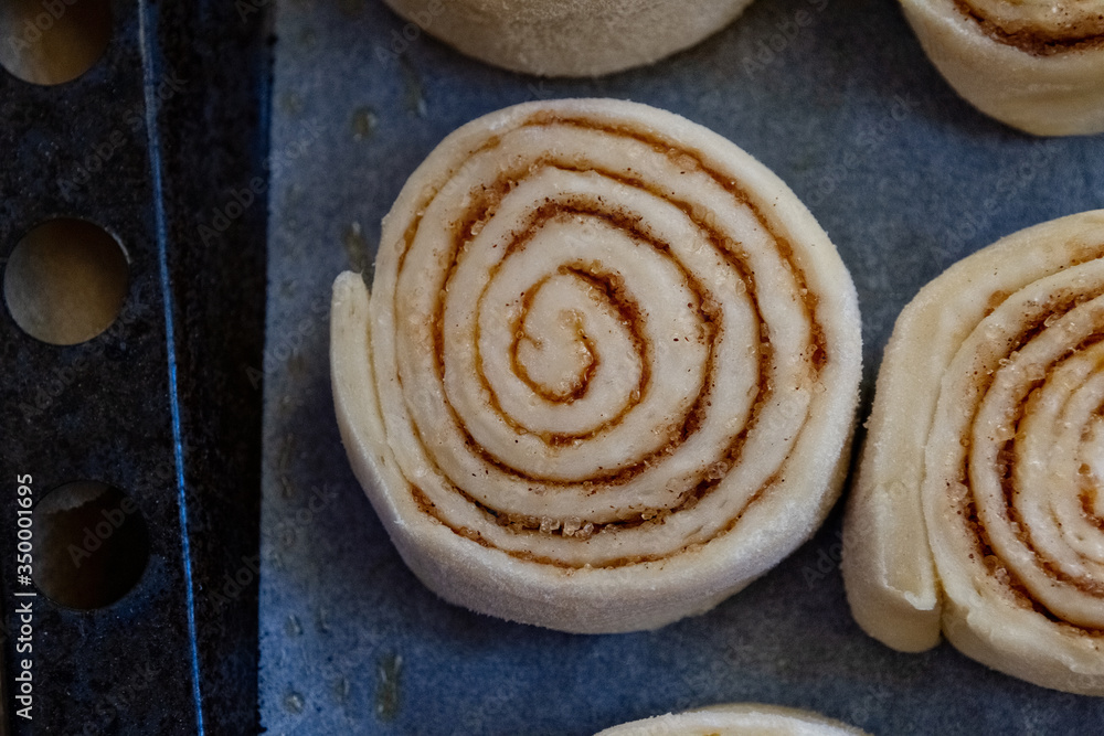 Fototapeta premium Dough buns cinnabon close up lie on baking sheet are ready for baking on row baking paper on blue background, side view