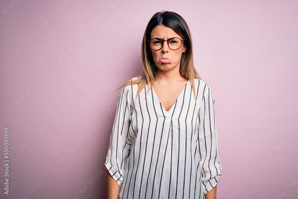 Young beautiful woman wearing casual striped t-shirt and glasses over pink background depressed and worry for distress, crying angry and afraid. Sad expression. Young beautiful woman wearing casual striped t-shirt and glasses over pink background depressed and worry for distress, crying angry and afraid. Sad expression.