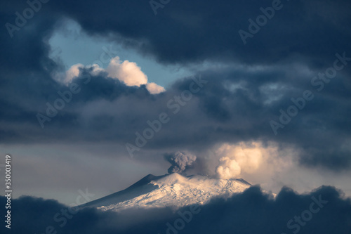 Snow Covered Etna Mountain Emit Smoke From Central Crater Framed By Stormy Low Clouds; The Volcano Is A Natural Landmark Of Sicily