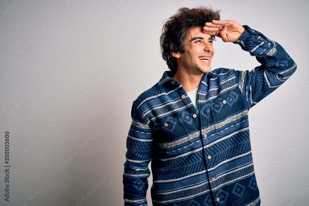 Young handsome man wearing casual shirt standing over isolated white background very happy and smiling looking far away with hand over head. Searching concept. Young handsome man wearing casual shirt standing over isolated white background very happy and smiling looking far away with hand over head. Searching concept.