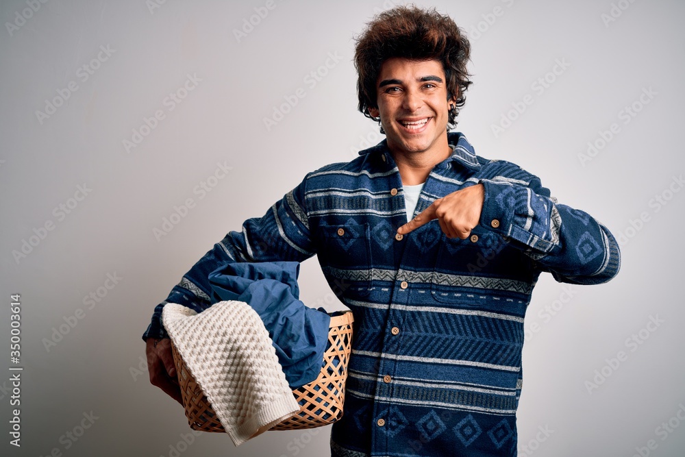 Young handsome man holding wicker basket with clothes over isolated white background very happy pointing with hand and finger Young handsome man holding wicker basket with clothes over isolated white background very happy pointing with hand and finger