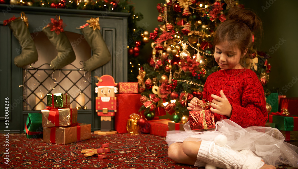 A little girl catches a flying gift smiles rejoices and waits for Christmas New Year and a holiday The cozy house, burning fireplace and a Christmas tree 