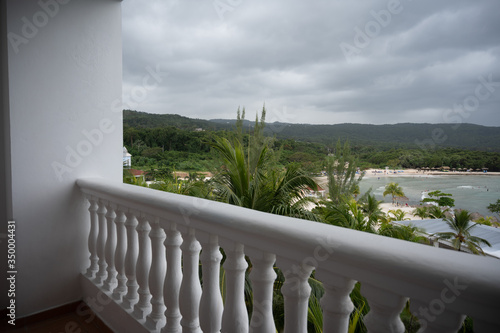 a white resort hotel balcony overlooks a tropical beach scene on a cloudy day