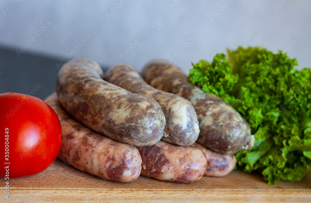 Raw homemade meat sausages with spices that lie on a wooden board near tomato and lettuce Raw homemade meat sausages with spices that lie on a wooden board near tomato and lettuce
