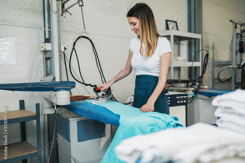 Obraz na płótnie Woman with iron working at ironing shop. Cleaning services.