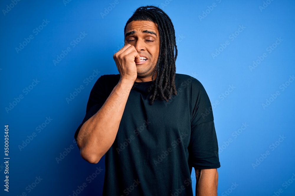 Young handsome african american afro man with dreadlocks wearing casual t-shirt looking stressed and nervous with hands on mouth biting nails. Anxiety problem. Young handsome african american afro man with dreadlocks wearing casual t-shirt looking stressed and nervous with hands on mouth biting nails. Anxiety problem.