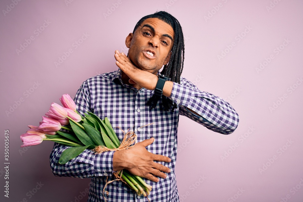 Young african american afro romantic man with dreadlocks holding bouquet of pink tulips cutting throat with hand as knife, threaten aggression with furious violence Young african american afro romantic man with dreadlocks holding bouquet of pink tulips cutting throat with hand as knife, threaten aggression with furious violence