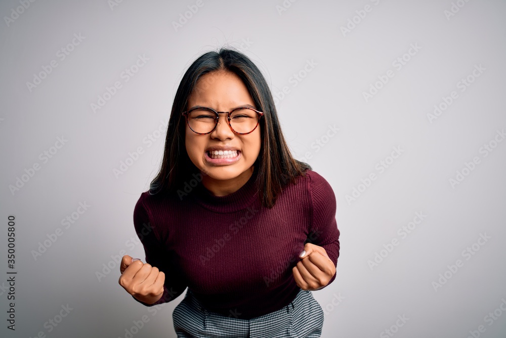 Beautiful asian business woman wearing casual sweater and glasses over white background very happy and excited doing winner gesture with arms raised, smiling and screaming for success. Celebration Beautiful asian business woman wearing casual sweater and glasses over white background very happy and excited doing winner gesture with arms raised, smiling and screaming for success. Celebration