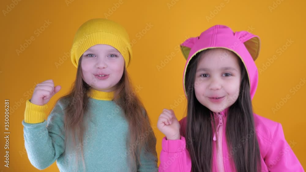 Two cheerful cute little girls laughing and having fun on a yellow background. The concept of friendship, entertainment and fashionable children clothing. Studio shot Two cheerful cute little girls laughing and having fun on a yellow background. The concept of friendship, entertainment and fashionable children clothing. Studio shot