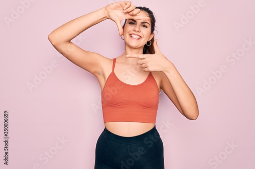 Young beautiful fitness woman wearing sport excersie clothes over pink background smiling making frame with hands and fingers with happy face. Creativity and photography concept. photo