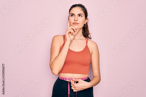 Young beautiful fitness woman wearing sport excersie clothes using measuring tape serious face thinking about question, very confused idea photo