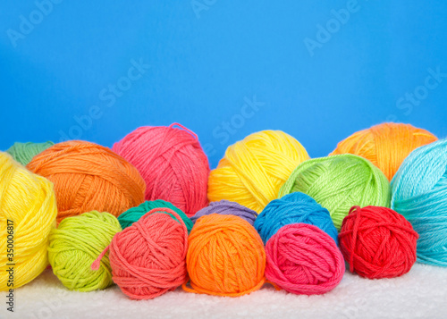 Many bright colorful balls of yarn laying on a blanket, bright blue background with copy space.