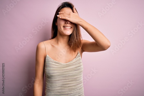 Young beautiful brunette girl wearing casual striped t-shirt over isolated pink background smiling and laughing with hand on face covering eyes for surprise. Blind concept.