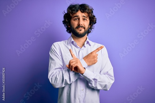 Young handsome business man with beard wearing shirt standing over purple background Pointing to both sides with fingers, different direction disagree