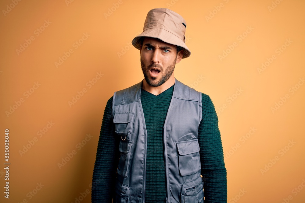Handsome tourist man with beard on vacation wearing explorer hat over yellow background In shock face, looking skeptical and sarcastic, surprised with open mouth Handsome tourist man with beard on vacation wearing explorer hat over yellow background In shock face, looking skeptical and sarcastic, surprised with open mouth