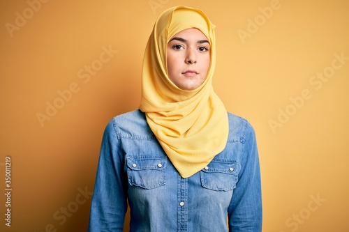 Young beautiful girl wearing muslim hijab standing over isolated yellow background Relaxed with serious expression on face. Simple and natural looking at the camera. © Krakenimages.com