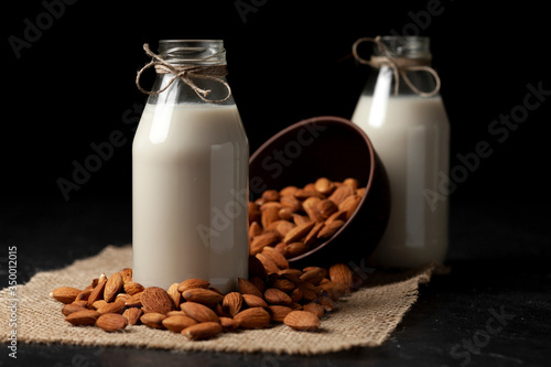 lactose-free almond milk in bottles with nuts on a black table, vegetarian milk drink, healthy milk product