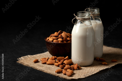 almond milk in bottles with nuts on a black table  a variety of dairy products without sugar and lactose  a vegetarian drink
