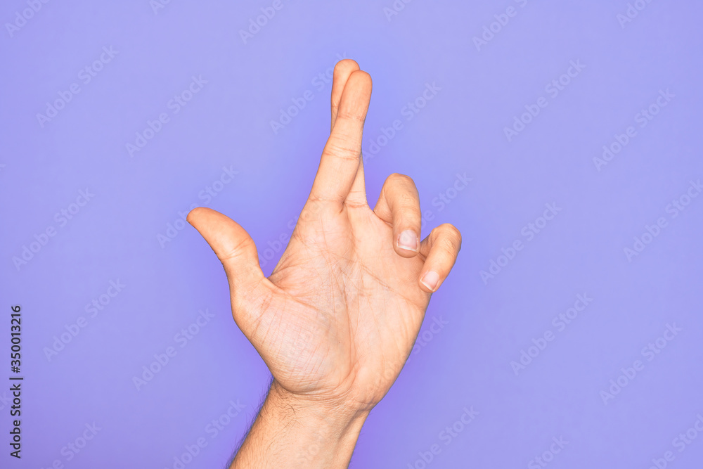 Hand of caucasian young man showing fingers over isolated purple background gesturing fingers crossed, superstition and lucky gesture, lucky and hope expression Hand of caucasian young man showing fingers over isolated purple background gesturing fingers crossed, superstition and lucky gesture, lucky and hope expression