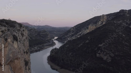 AERIAL DRON SIDE MOVEMENT IN MOUNTAIN RANGE CLIFF AND RIVER REVEAL IN STUNNING CAYON, SUN SET IN San Lorenzo de Montgai, CATALONIA, SPAIN