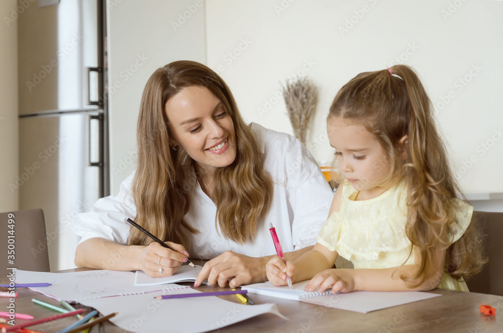 Little daughter doing homework at home with mother. Little daughter doing homework at home with mother.