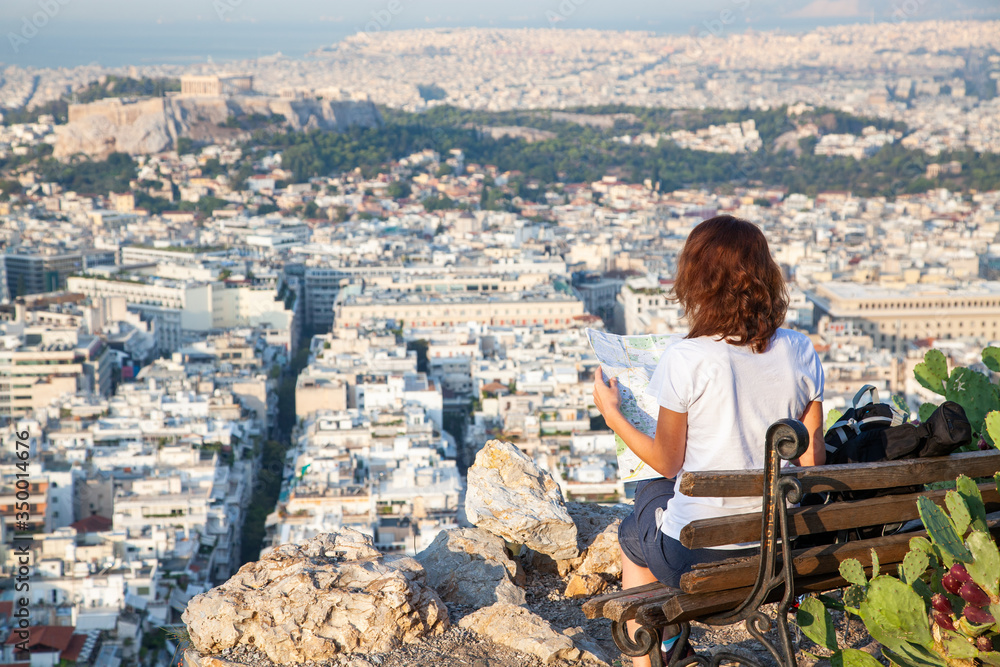 woman with a map sitting on Lycabettus Hill, the highest point in the city overlooking Athens with the Acropolis - world traveller