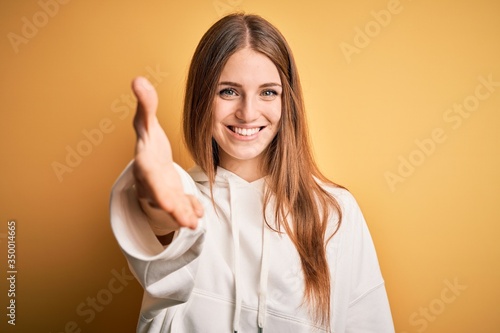 Wallpaper Mural Young beautiful redhead sporty woman wearing sweatshirt over isolated yellow background smiling friendly offering handshake as greeting and welcoming. Successful business. Torontodigital.ca