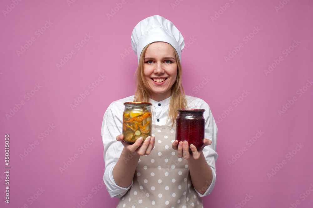 cheerful girl cook in kitchen clothes holds canned food and smiles on a colored background, woman housewife with food blanks