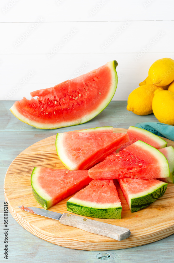 Slices of watermelon and lemons on a wood cutting board and wooden background