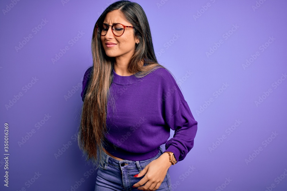 Young beautiful smart woman wearing glasses over purple isolated background Suffering of backache, touching back with hand, muscular pain Young beautiful smart woman wearing glasses over purple isolated background Suffering of backache, touching back with hand, muscular pain